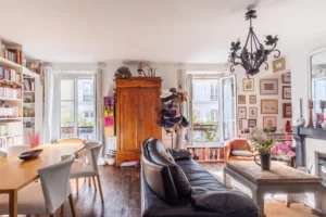 Séjour lumineux avec bibliothèque, parquet en bois ancien et grandes fenêtres dans un appartement à vendre Paris 18 Montmartre