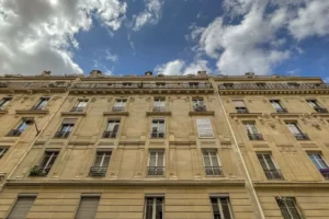 Façade haussmannienne typique avec balcons filants et ciel nuageux.