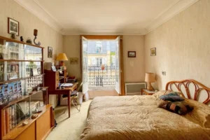Chambre principale spacieuse avec lit double, coin bureau et accès au balcon.