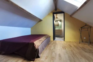 Chambre d’amis sous combles avec mur jaune et parquet bois clair