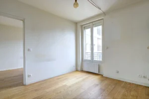 Pièce principale avec fenêtre double vitrage et mur à repeindre, ouverte sur la chambre.