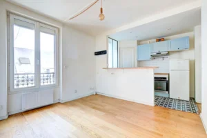 Pièce de vie principale avec cuisine semi-ouverte, parquet au sol et lumière naturelle.