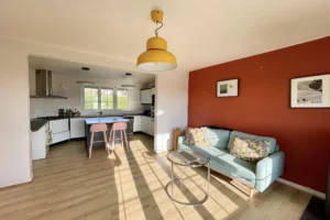Coin salon chaleureux avec lumière naturelle, parquet et mur terracotta à Pont-l’Évêque.