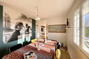 Salle à manger baignée de lumière naturelle avec décoration murale originale à Pont-l’Évêque.