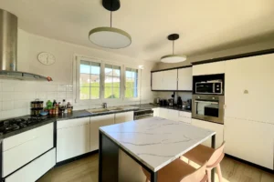 Cuisine équipée avec ilot central, électroménagers encastrés et vue sur le jardin à Pont-l’Évêque.
