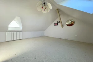Espace sous-pente lumineux avec radiateur et fenêtre triangulaire, chambre à Pont-l’Évêque.