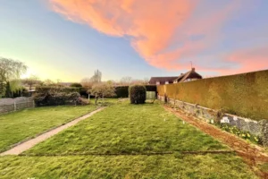 Jardin clos et arboré avec ciel coloré au crépuscule, maison à vendre à Pont-l’Évêque.