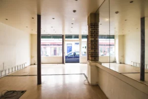 Vue intérieure d’un local commercial à Paris 19ᵉ avec colonne en brique, parquet clair et grande vitrine sur rue.
