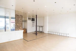 Espace principal d’un local commercial à Paris 19ᵉ, avec parquet clair, mur en brique apparente et belle luminosité.