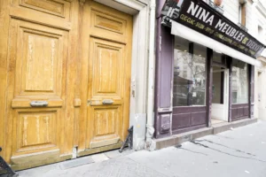 Façade extérieure d’un local commercial à Paris 19ᵉ, avec vitrine sur rue passante et porte cochère en bois massif.