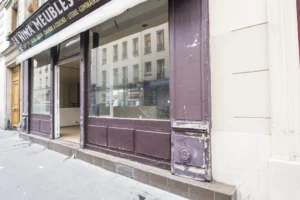 Façade sur rue d’un local commercial à Paris 19ᵉ, vitrine en bois à rénover donnant sur une rue passante du quartier Jaurès.