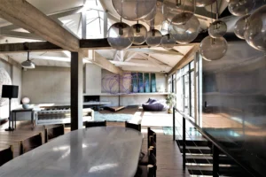 Vue d’ensemble spectaculaire d’un loft lumineux à Bagnolet, avec poutres apparentes, verrières industrielles, mobilier design et volumes généreux baignant dans la lumière naturelle.