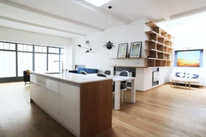 Vue principale du loft à vendre Paris 10, avec cuisine ouverte, salon lumineux, verrière atelier et bibliothèque sur mesure – quartier Cours de la Ferme Saint-Lazare / Marché Saint-Quentin.