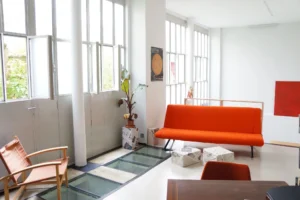 Vue d’un salon lumineux avec verrières d’atelier, canapé orange et sol en verre, dans un loft à vendre à Paris 10, secteur Porte Saint-Denis.