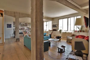 Loft lumineux au cœur du 10ᵉ arrondissement de Paris, avec grande pièce de vie, poutres en béton brut, parquet ancien et mobilier éclectique, situé rue de Chabrol, proche du marché Saint-Quentin.
