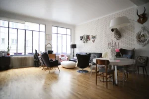 Vaste salon lumineux au style éclectique avec mur en briques blanches, grandes verrières et parquet en chêne, situé rue du Faubourg Saint-Denis à Paris 10ᵉ.