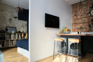 Vue d’un appartement à Montmartre Pais 18 avec cuisine au style loft et chambre semi-ouverte, mur en pierre, parquet bois clair et mobilier chaleureux.