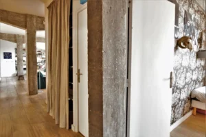 Espace de circulation entre chambres dans un loft à Paris 10ᵉ, avec poutres béton, rideaux naturels et papier peint à motifs.