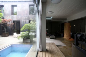 Vue sur la cour intérieure d’un loft à Bagnolet avec bassin, terrasse en bois, arbres en pot et ouverture vers un espace bureau design.