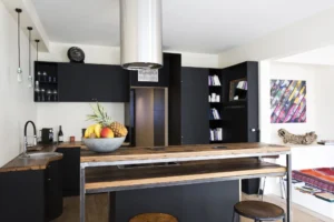 Cuisine noire et bois avec vue sur le salon coloré, dans une maison au design unique à Paris 15.