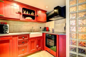 Cuisine originale du loft à Paris 17 – Meubles rouges, crédence en pierre claire, verrière en briques de verre et équipements modernes.