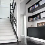Escalier blanc avec garde-corps noir dans un loft parisien, espace bureau avec bibliothèque intégrée et architecture soignée, quartier Faubourg Saint-Denis, Paris 10ᵉ.