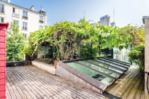 Toit-terrasse arboré avec verrière zénithale, végétation abondante et pergola naturelle en cœur d’îlot à Paris 18.