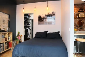 Chambre avec dressing dans un appartement à vendre à Montmartre Paris 18, mur en pierre, déco murale et suspension industrielle dans un espace optimisé.