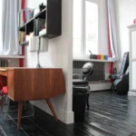 Chambre lumineuse dans un loft parisien, coin bureau au design vintage, étagères murales, fauteuil design et rangements intégrés, Paris 10ᵉ arrondissement.