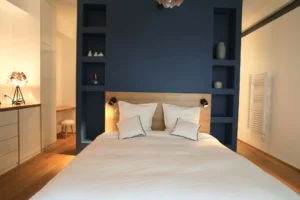 Chambre parentale avec tête de lit encastrée bleue nuit, éclairages intégrés et aménagements sur mesure dans un loft à Paris 10.