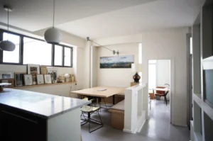 Coin repas lumineux avec banquette intégrée, table en bois, œuvres encadrées et vue vers un bureau, dans un appartement à vendre Paris 10ᵉ rue Martel.