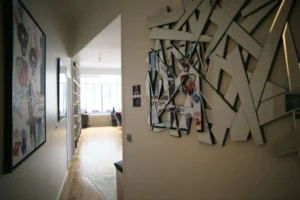 Couloir d’entrée avec miroir mural artistique et vue dégagée sur le séjour baigné de lumière naturelle dans un loft à Paris 10ᵉ.