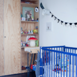 Chambre de bébé avec lit à barreaux bleu, étagères ouvertes en bois brut et objets de décoration ludiques dans un loft à vendre à Paris 10ᵉ, rue du Faubourg Saint-Denis.