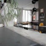 Zoom sur un plan de travail en béton brut dans un loft à Paris 10, avec suspension design, plantes retombantes et lumière naturelle filtrée par de grandes fenêtres.