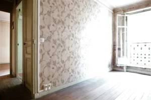 Pièce lumineuse avec double exposition, parquet ancien, papier peint d’origine et vue sur une fenêtre à garde-corps, dans un appartement à rénover à Paris 19e, secteur Belleville.