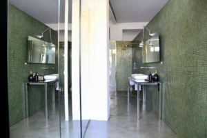 Salle de bain contemporaine, avec murs en mosaïque verte, double vasque sur structure en inox et éclairage directionnel.