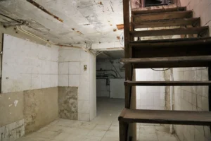 Sous-sol du local commercial avec escalier bois, murs carrelés, potentiel de stockage ou cuisine.