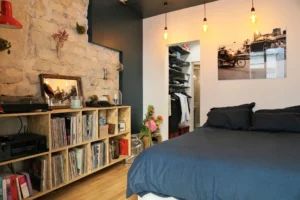 Chambre d’un appartement à Montmartre Paris 18 avec mur en pierre naturelle, étagère à vinyles, dressing ouvert et ambiance chaleureuse.