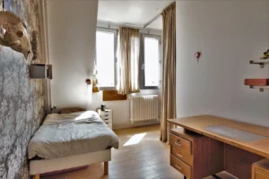 Chambre d’enfant ou d’adolescent dans un loft à Paris 10ᵉ, avec bureau en bois, lit simple, papier peint, et trois fenêtres apportant une belle luminosité.