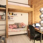 Chambre avec mezzanine en bois, mur en briques apparentes et coin bureau aménagé dans un loft familial à Paris 10ᵉ.