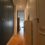 Vue en perspective du couloir d’entrée, avec éclairages intégrés, plafond sombre et parquet bois clair dans un loft parisien.