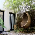 Patio végétalisé avec bambous, sol en pavés anciens et fauteuil suspendu en rotin, offrant un espace extérieur apaisant.