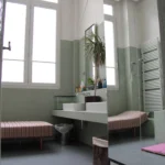 Salle de bains lumineuse avec grande fenêtre, double vasque, pare-douche en verre et banc tapissé dans un loft du 10ᵉ arrondissement de Paris.