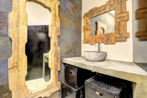 Salle d’eau du loft à Paris 17 – Vasque en pierre naturelle, béton ciré, miroirs en bois brut et murs texturés pour une ambiance authentique.
