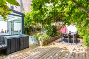 Terrasse baignée de lumière, avec coin repas, cabanon coloré et vue sur véranda vitrée du loft.