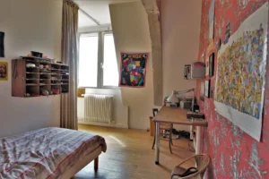 Chambre d’adolescent dans un loft à Paris 10ᵉ, avec bureau, lit simple, papier peint rouge illustré et grande fenêtre sur cour.