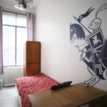 Petite chambre d’enfant lumineuse avec lit simple, armoire en bois et fresque murale originale dans un loft situé à Paris 10ᵉ.