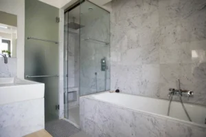 Salle de bain en marbre avec baignoire encastrée, douche à l’italienne et finitions haut de gamme, dans un appartement à vendre à Paris 10ᵉ, rue Martel.