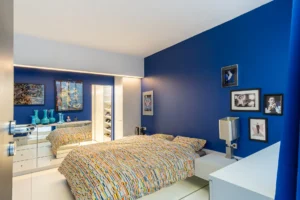 Chambre parentale aux murs bleus intenses, avec dressing intégré, miroir et décoration artistique contemporaine.