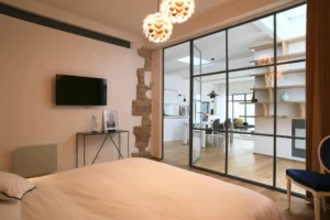 Chambre avec verrière sur salon, mur en pierre apparente, suspension lumineuse design et vue traversante dans un loft à Paris 10.
